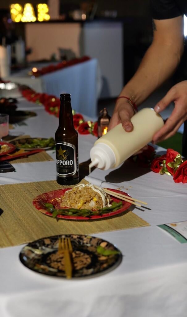 Hibachi chef adding sauce to a plate of noodles at a party table
