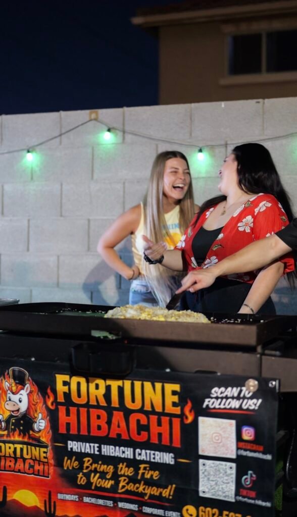 Two guests laughing behind the Fortune Hibachi grill at a backyard party
